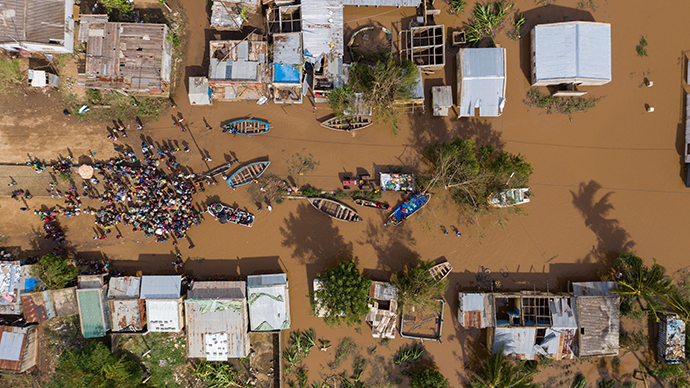 Overhead photo from a drone showing flooding, buildings and people gathering in a group with boats