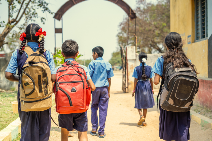 A group of children with backpacks on walking on a dusty road in a warm country