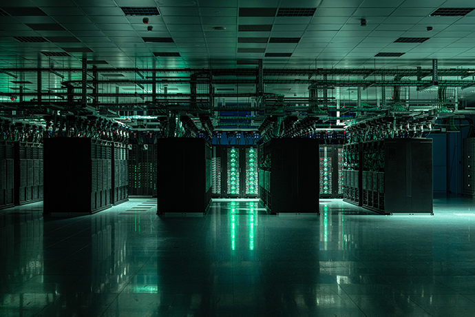 Rows of high-performance computing servers in ECMWF's data centre in Bologna, Italy, with illuminated server racks, overhead cabling and a reflective floor, supporting large-scale weather and climate modelling.