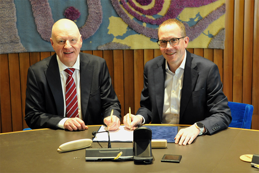 Roar Skålin and Florian Pappenberger sat at a table both signing a paper while smiling at the camera