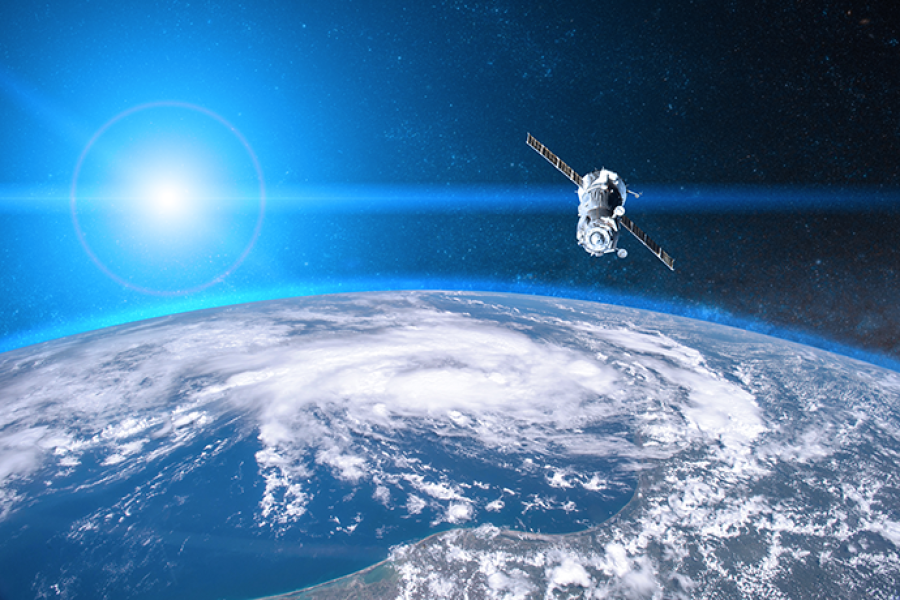 Satellite orbiting above Earth with cloud-covered weather systems visible below against the backdrop of space.