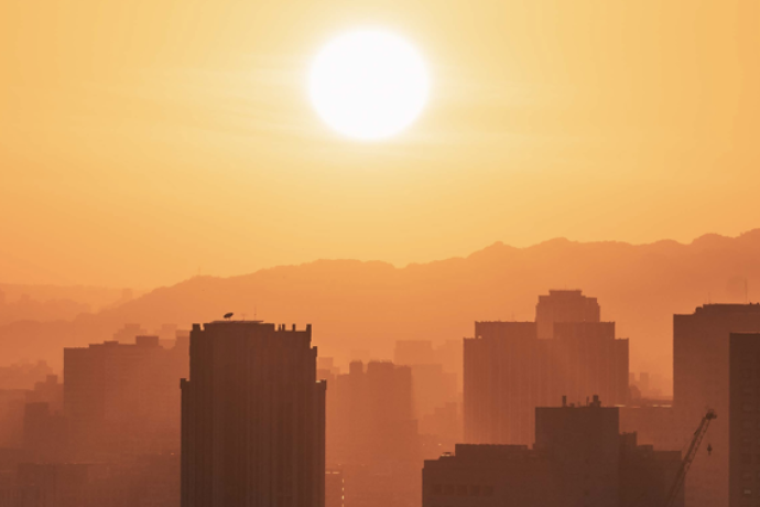 Urban skyline under extreme heat, with a bright sun and hazy atmosphere illustrating hot, potentially heat-stressful conditions.