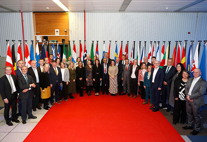 Group of approximately 36 people stood on a red carpet in front of flags