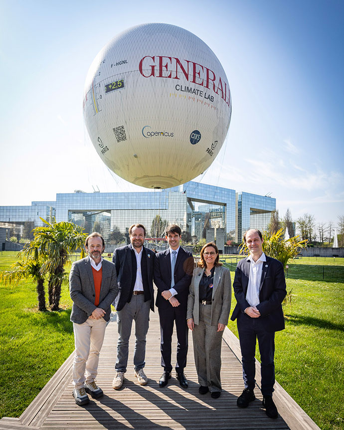 Five people stood on a path in fron of the Ballon de Paris. The balloon displays a large Generali logo