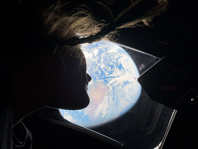Astronaut looking out the window of Orion at a brightly lit Earth
