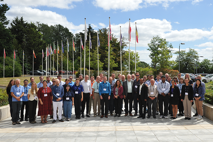 Large group of people on a patiod area in front of flag poles