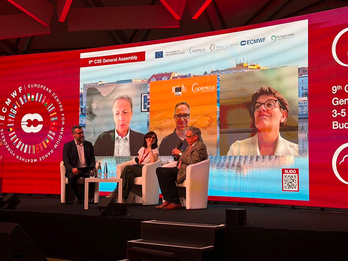 Panel discussion at the Copernicus Climate Change Service General Assembly, with three speakers on stage and remote participants displayed on a large screen behind them.