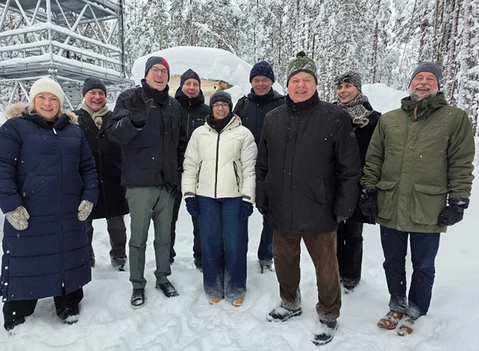 Group of nine people stood in a bunched up row in the snow all wearing thick jacets and hats