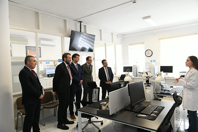 Five people in suits in a white lab speaking to another person in a lab coat
